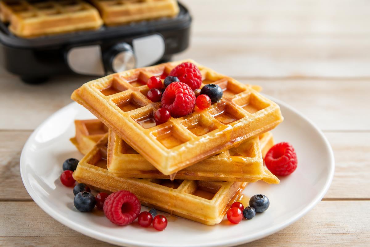 Gaufres healthy dorées empilées dans une assiette avec fruits rouges et filet de miel