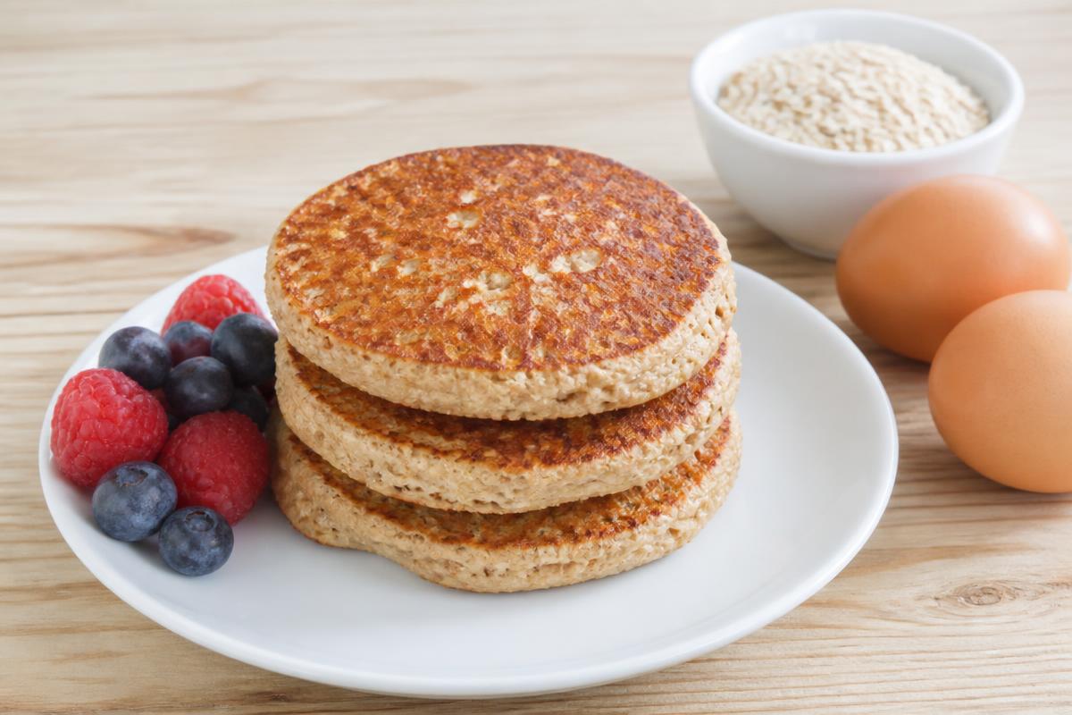 Trois crêpes épaisses à la farine d'avoine empilées, fruits rouges, œufs et avoine